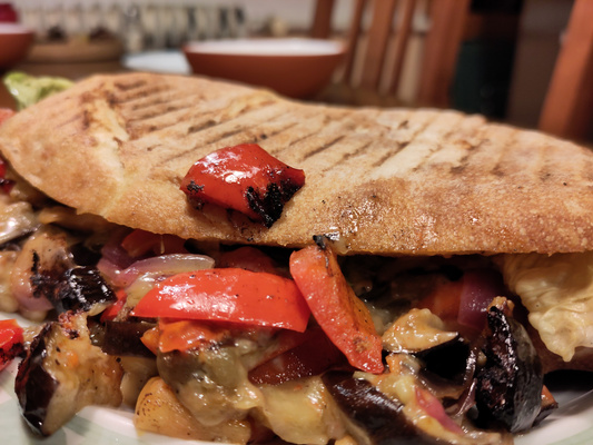 KI generiert: Ein gegrilltes Sandwich mit Gemüsefüllung, darunter rote Paprika und Auberginen.